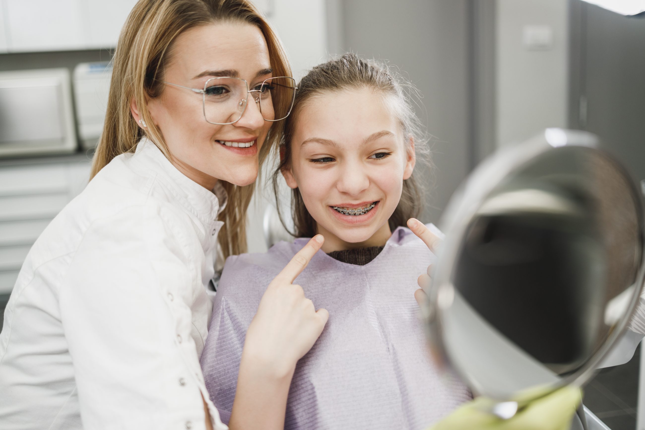 A teenage girl checking her smile in a mirror with a team member