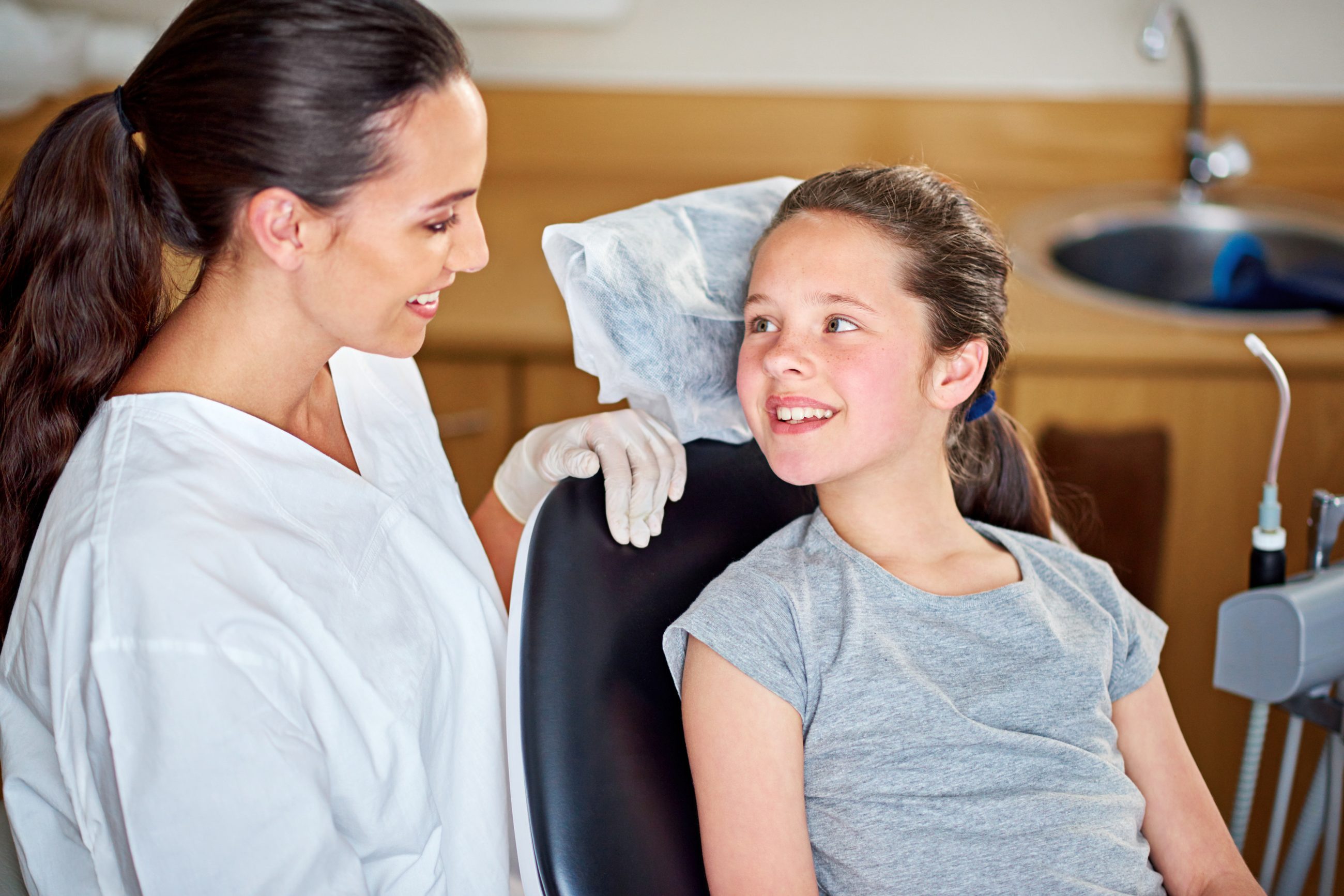 A smiling girl in the treatment chair talking with a team member