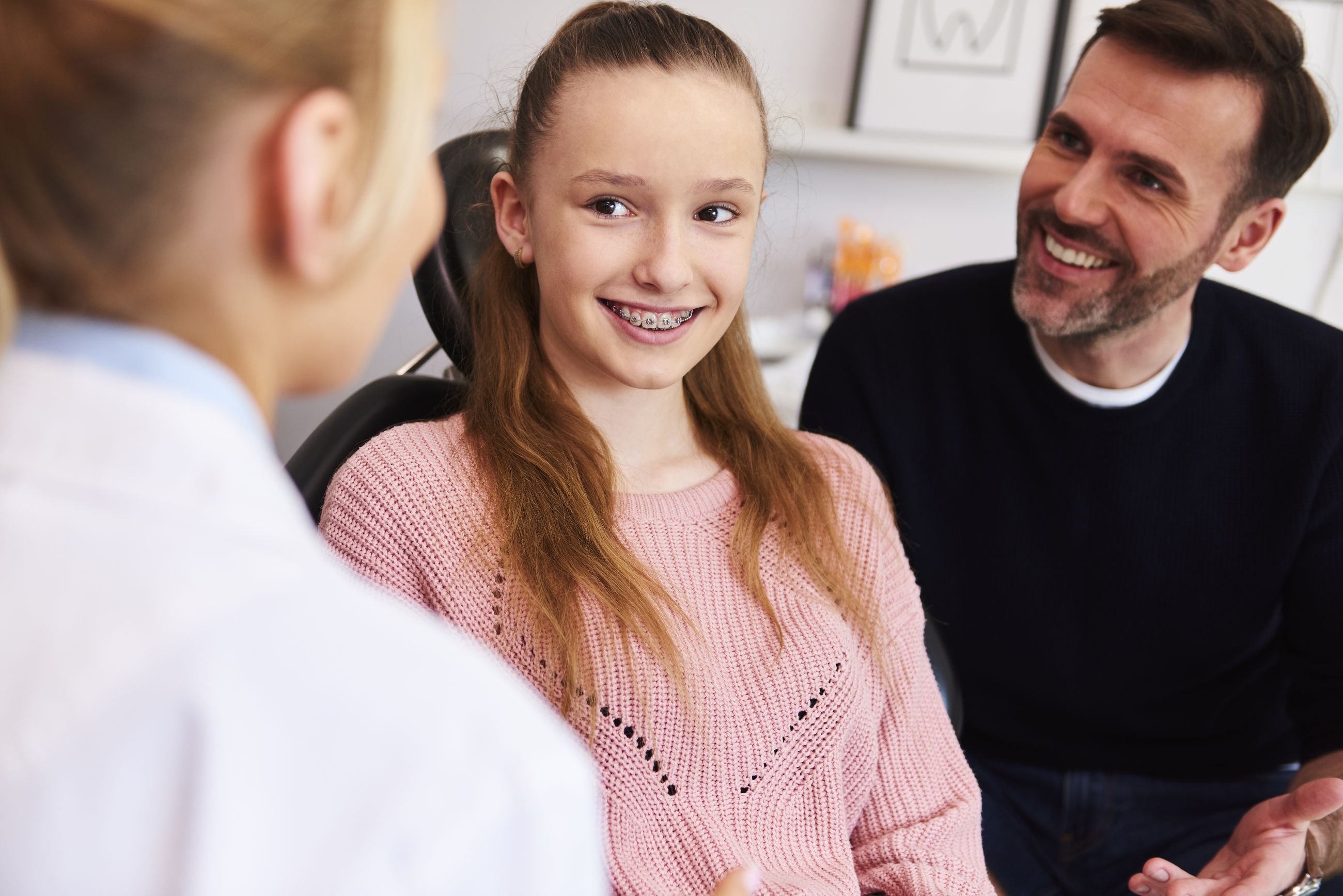 A smiling girl and her dad talking with an orthodontic team member