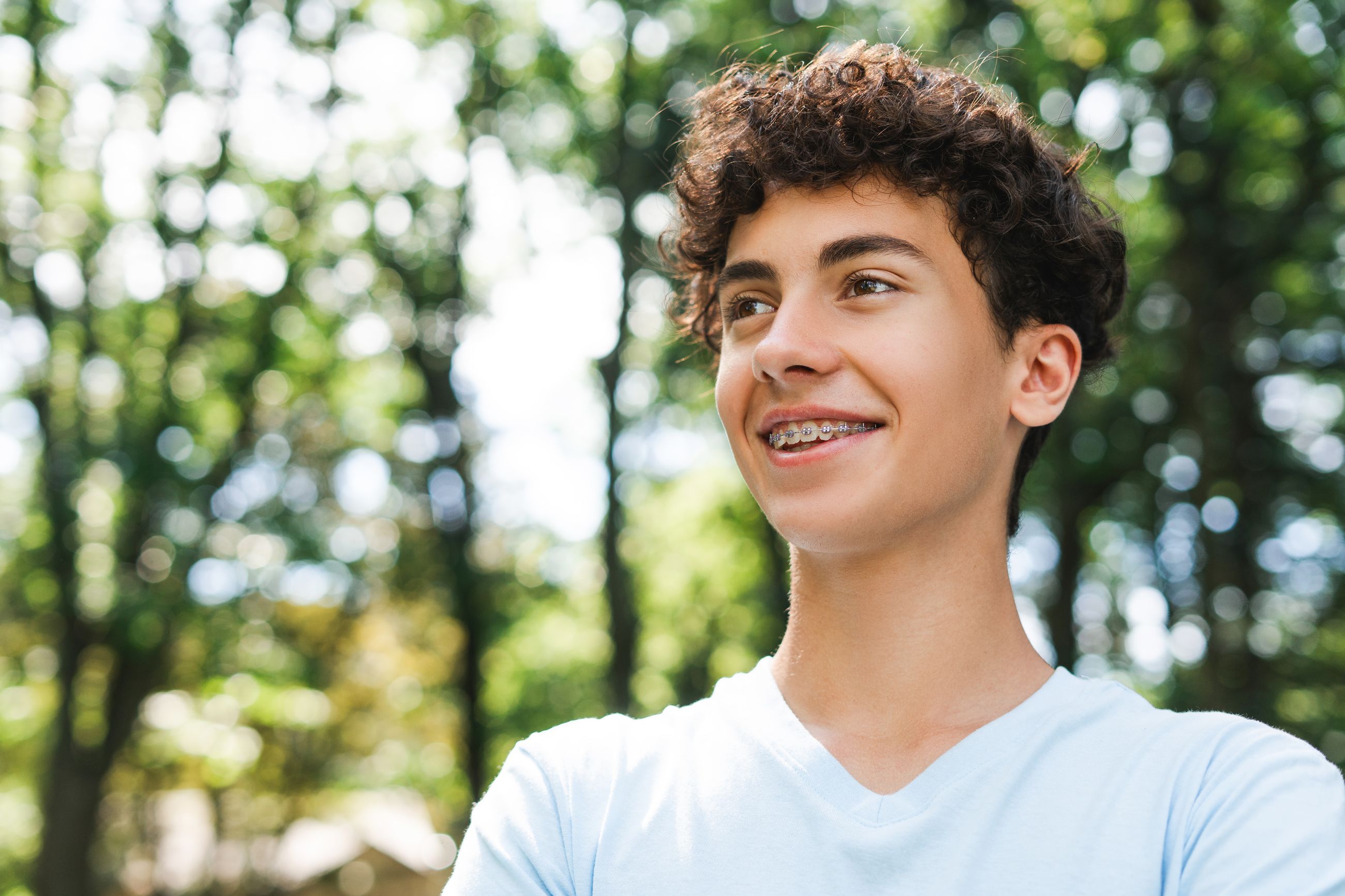 A smiling teenage boy with braces outdoors in a park